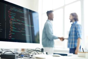 Two developers shaking hands in front of a code monitor, symbolizing staff augmentation and tech team collaboration in software development.